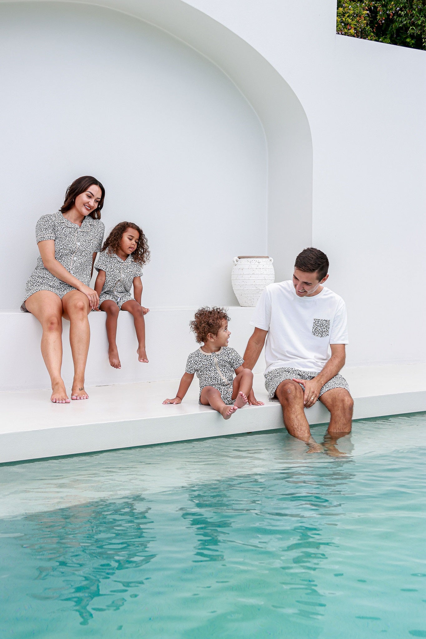 Family sitting down next to a pool, dressed in matching outfits, enjoying a sunny and relaxed day together.