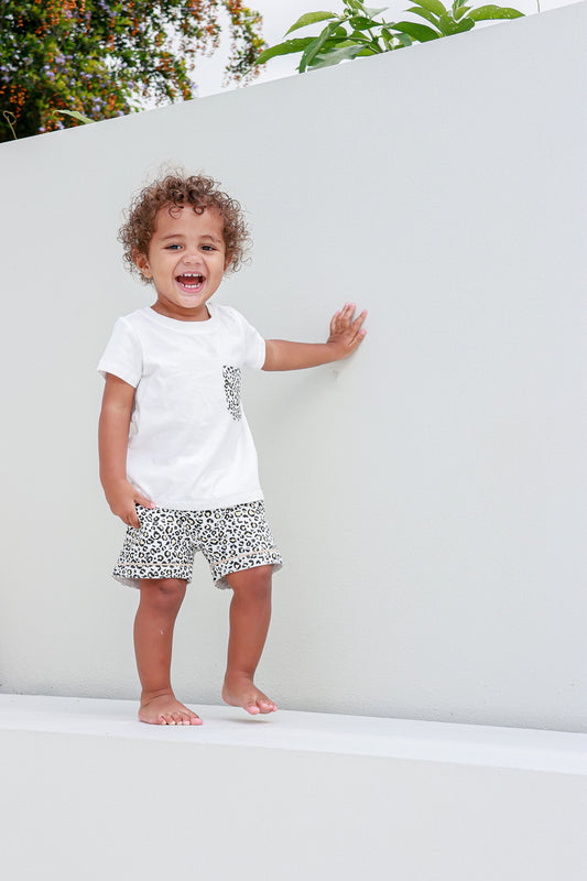 Kid smiling and wearing a leopard print pocket tee, radiating joy and casual style