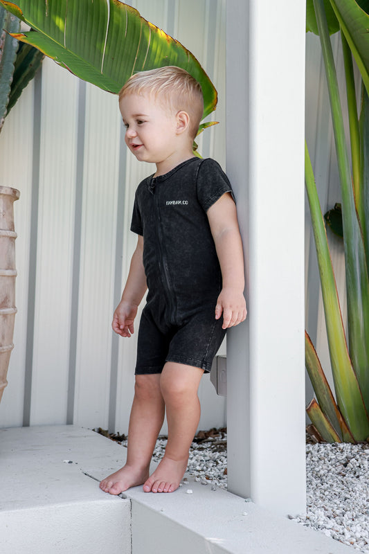 Boy toddler in logo acid wash romper standing leaning of post