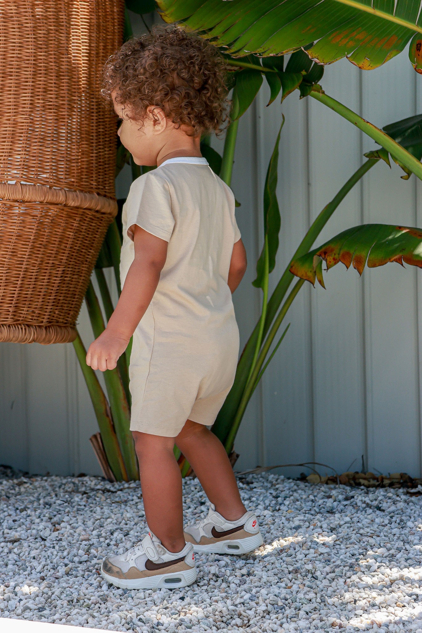 Toddler boy wearing logo beige romper standing