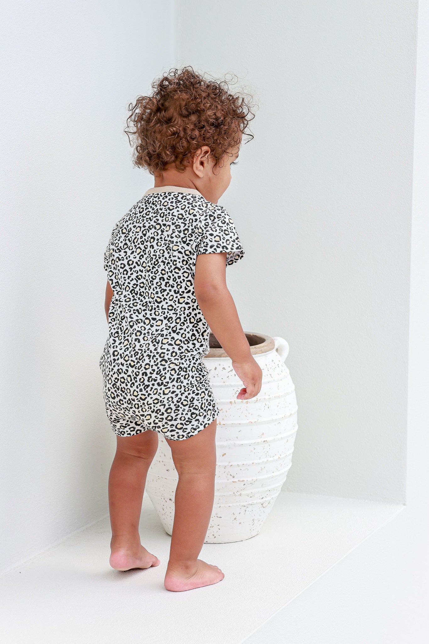 toddler boy standing next to vase wearing leopard print romper pyjamas