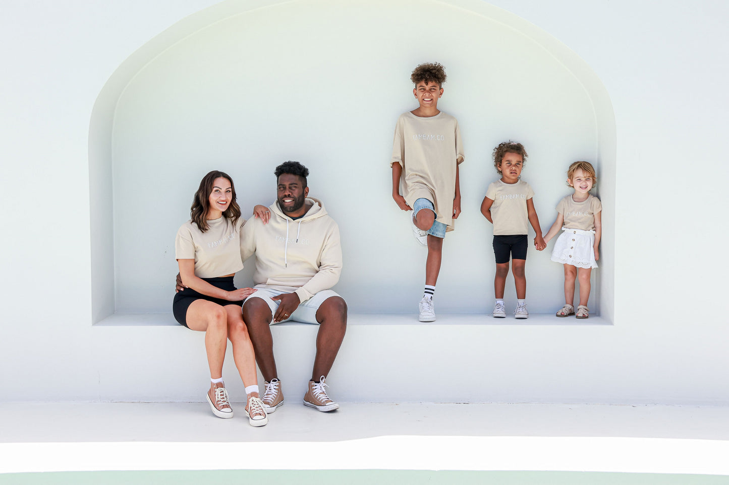family wearing matching beige shirts sitting and standing on arch seat