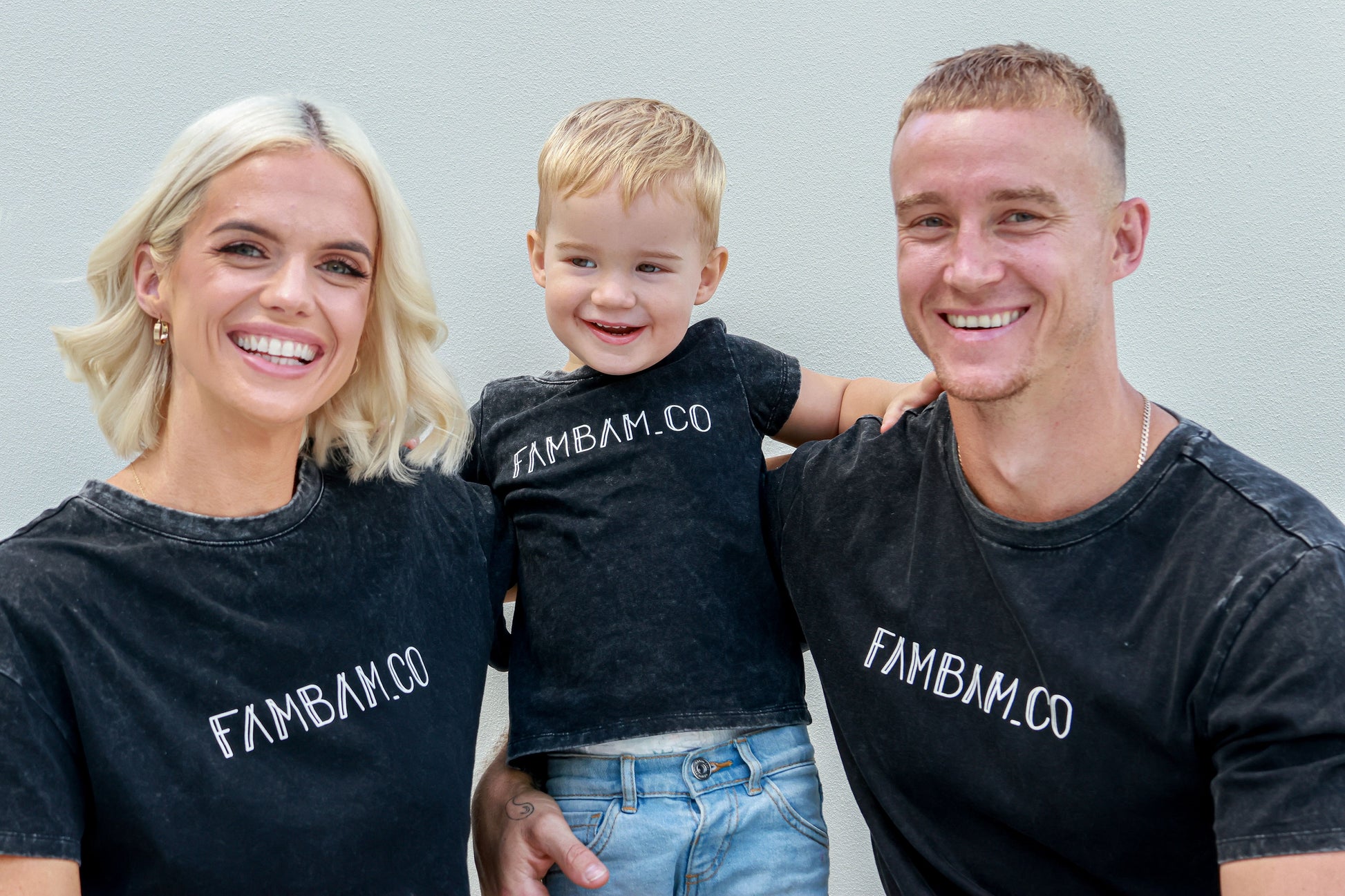 A family mum, dad and boy wearing matching acid wash logo shirt cuddling each other
