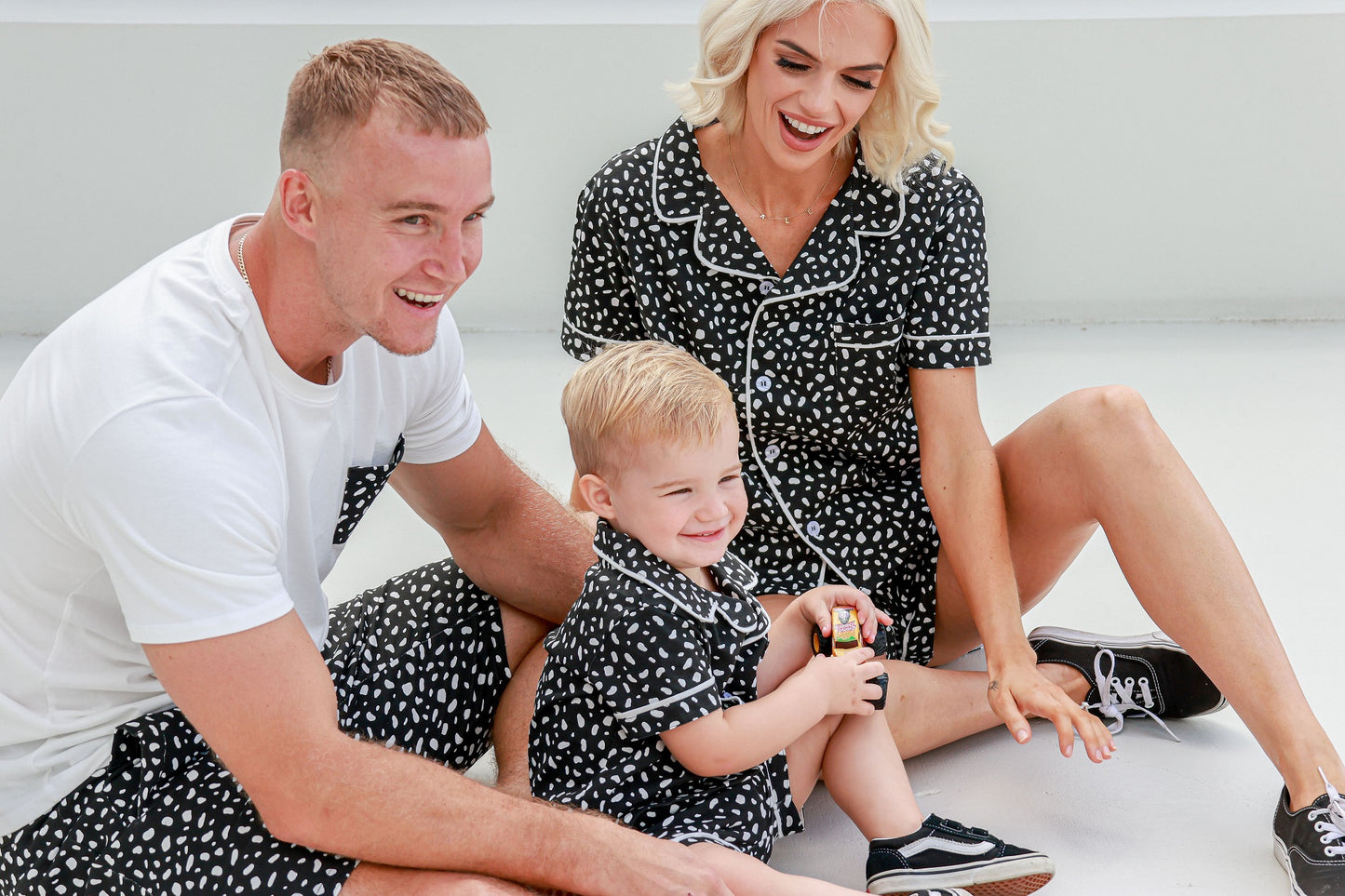 Family sitting down and playing with their son, all wearing matching pajamas, sharing a fun and cozy moment together.