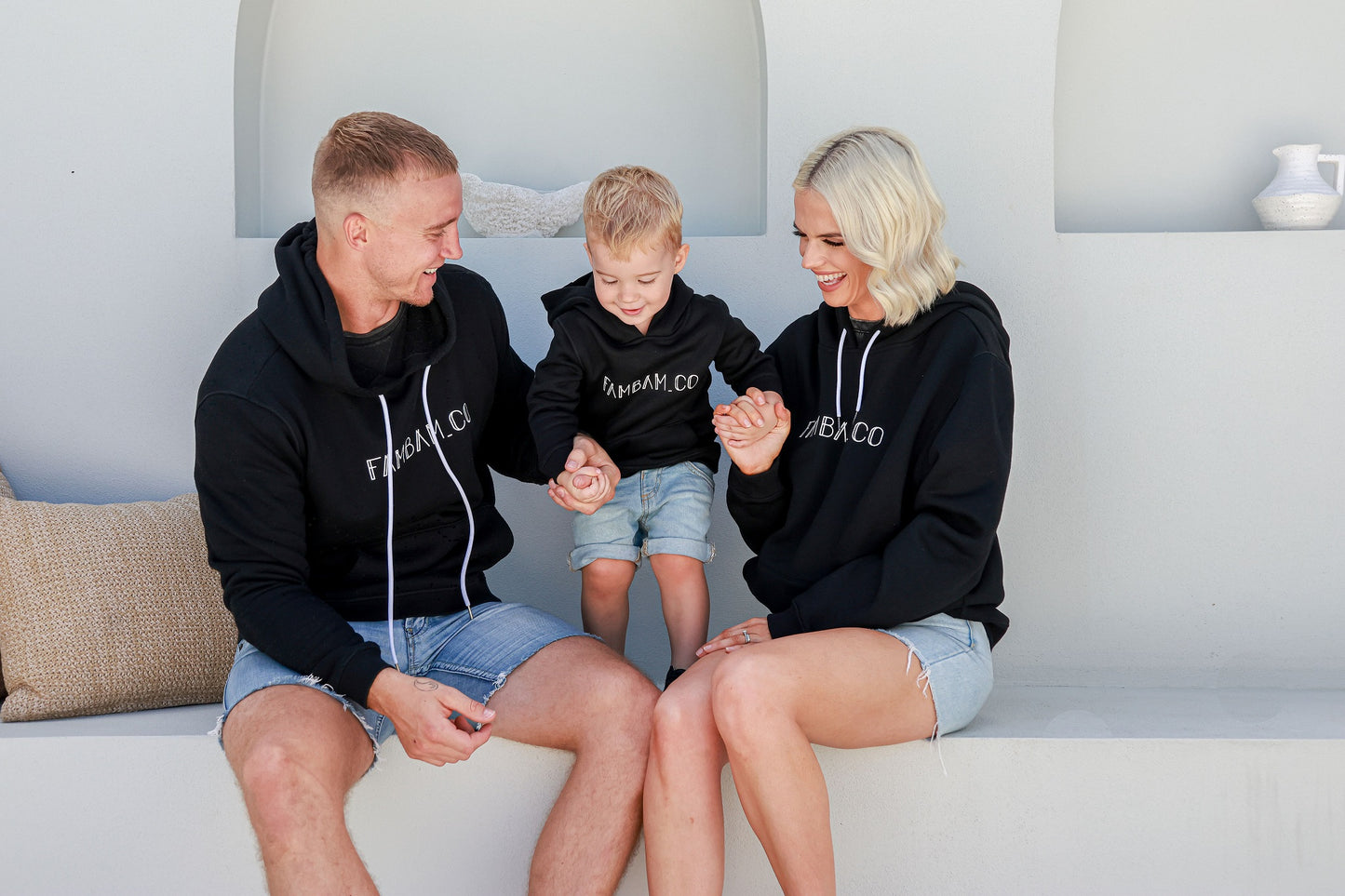 Father, mother, and son sitting together, all wearing matching black hoodie jumpers, enjoying a cozy and stylish family moment.