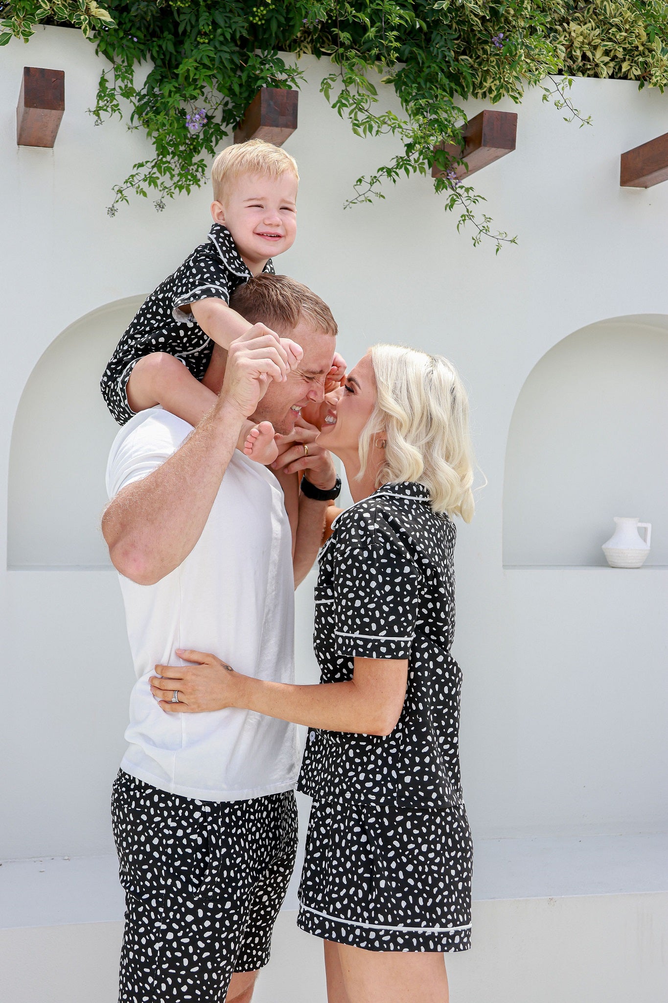 Mum and dad laughing together while son is on dads shoulders matching in white and black spotted pyjamas pjs pajamas
