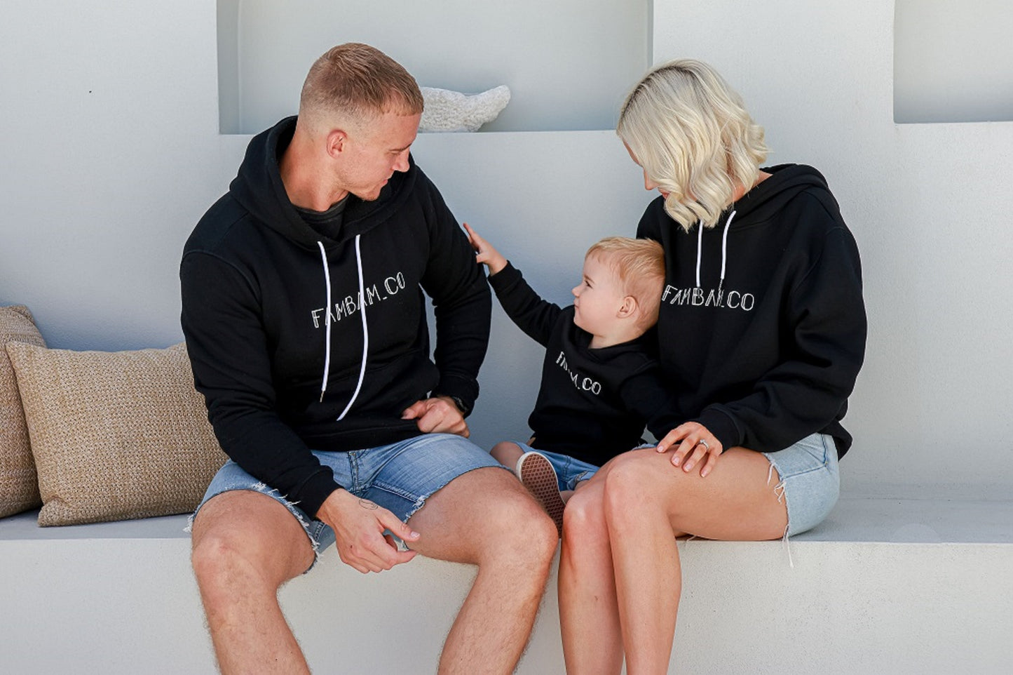 Father, mother, and son sitting together, all wearing matching black hoodie jumpers, enjoying a cozy and stylish family moment.