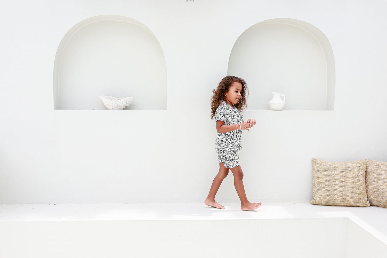 Girl walking past a white arched wall, wearing piped leopard print pajamas, combining style and comfort.