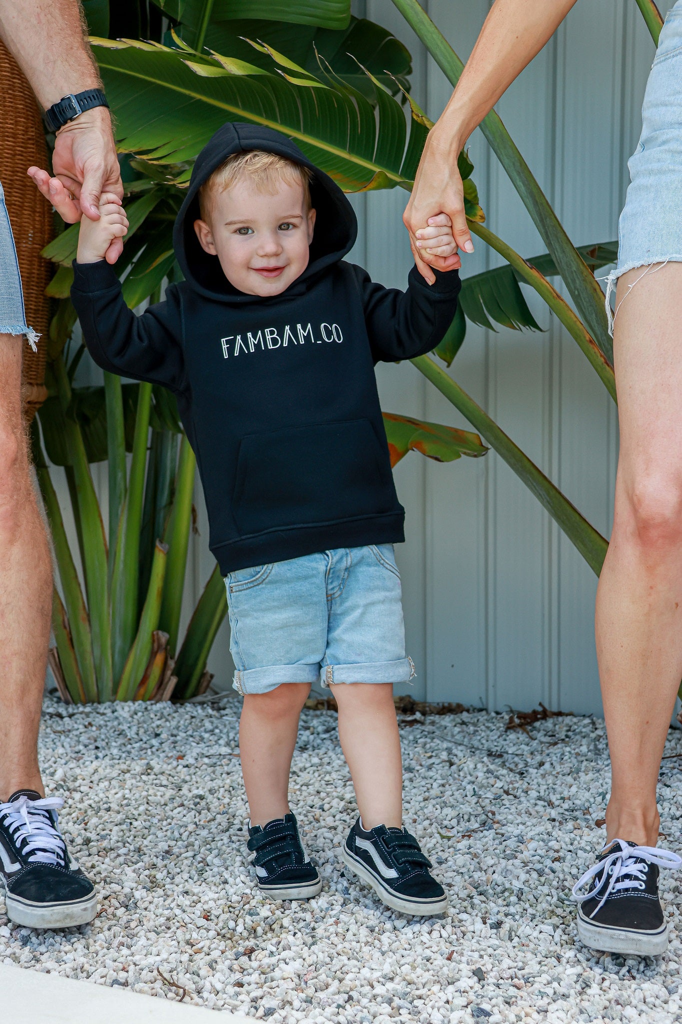 Toddler boy holding hands with mum and dad smiling wearing black jumper