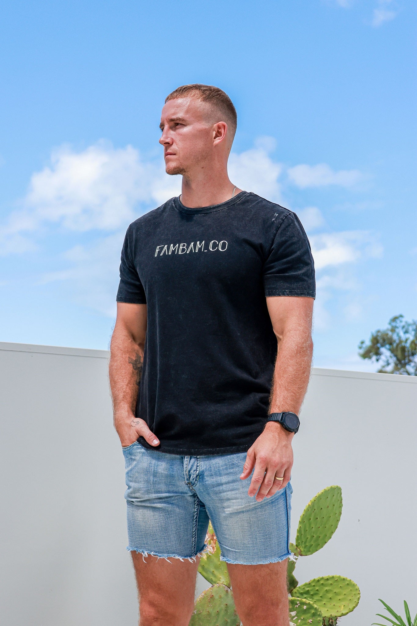 Man wearing acid wash logo shirt standing in front of cactus