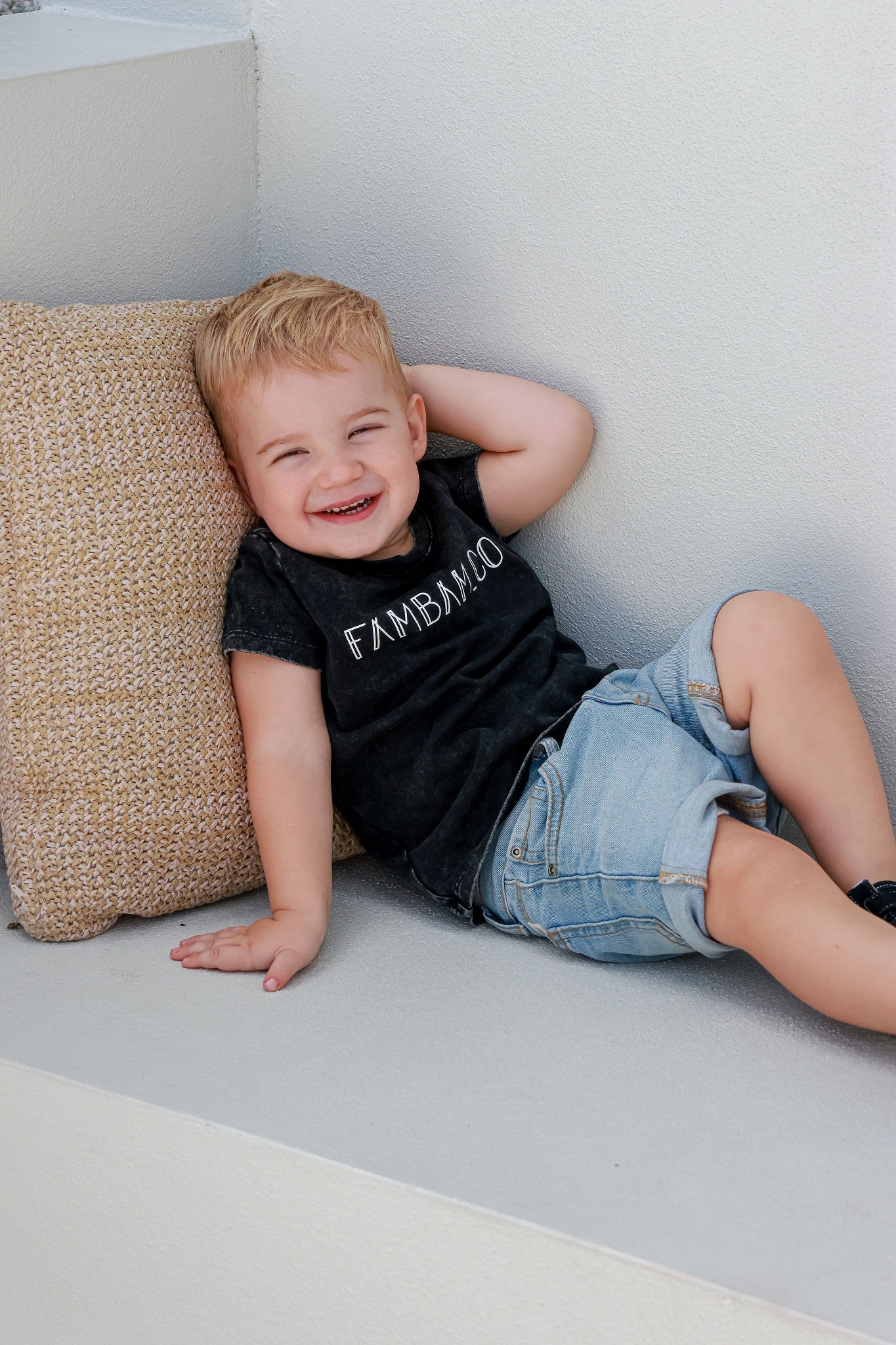 Toddler boy in logo acid wash shirt laying down on seat and a pillow