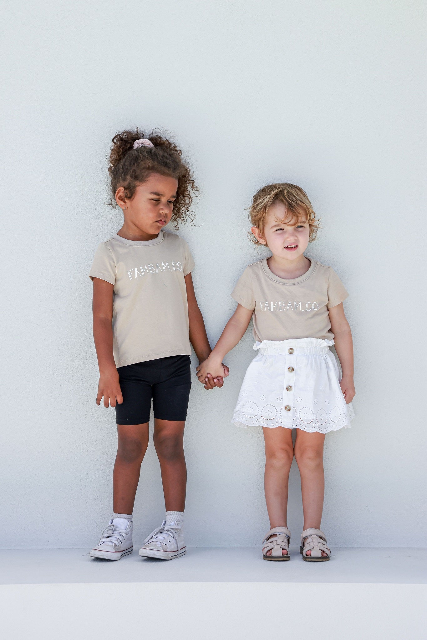 two girls holding hands in matching logo shirts in beige