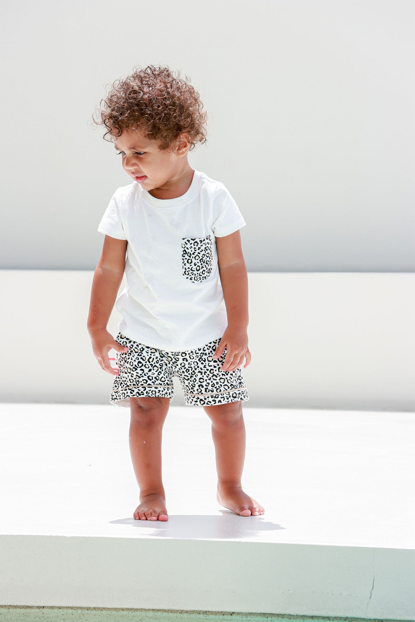Kid sitting comfortably in a leopard print pocket tee, showcasing a casual and playful style.