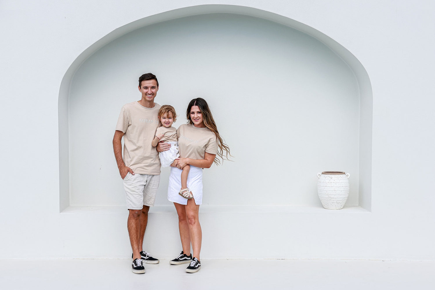 mum, dad and daughter posing for photo in front of arched wall