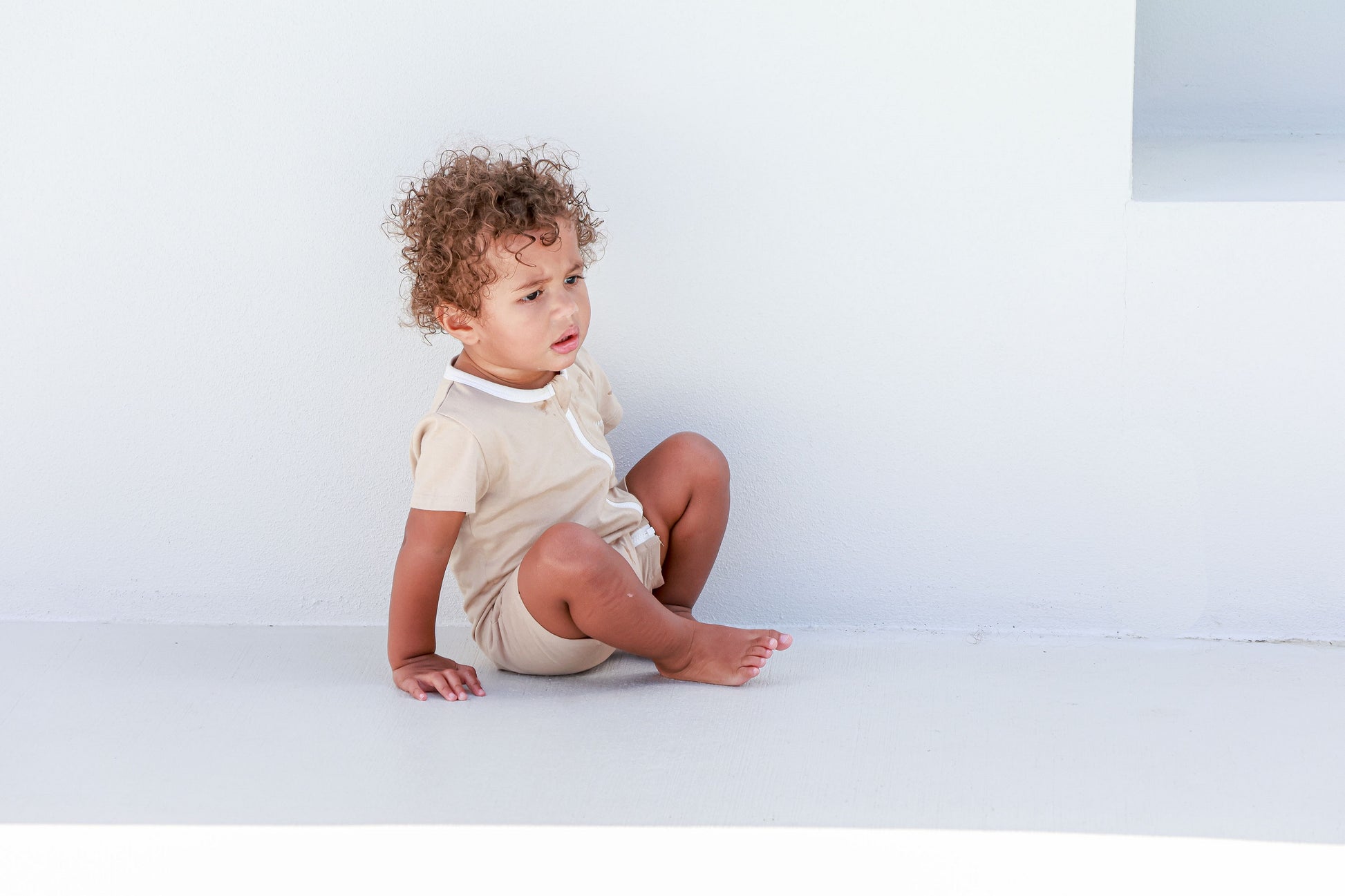 Toddler boy wearing logo beige romper sitting on white step