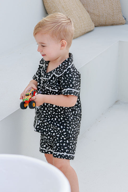 boy playing with toy truck while wearing white nad black spotted pyjama set