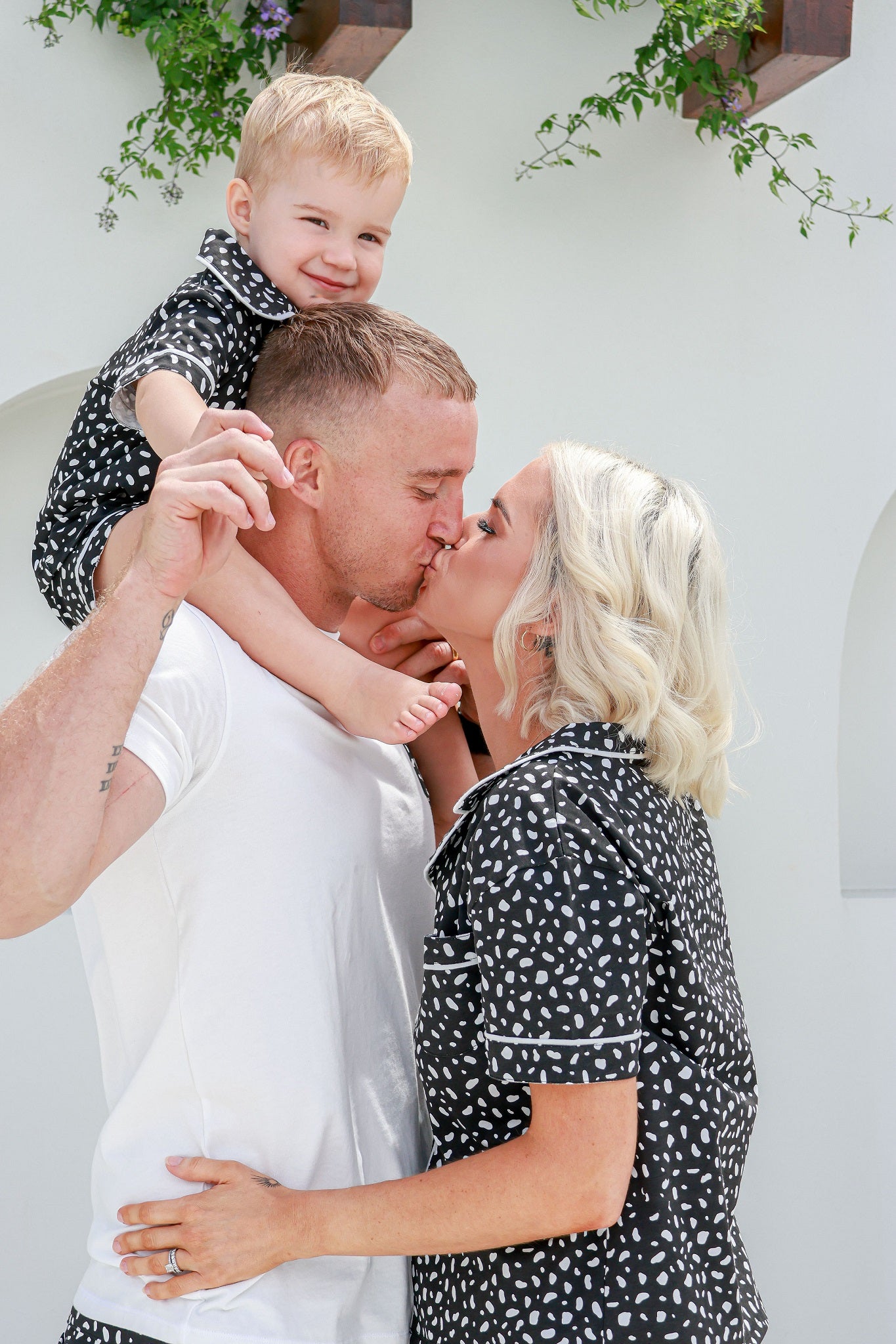 Mum and dad kissing while dad has son on shoulders all wearing matching pyjamas PJ's pajamas 