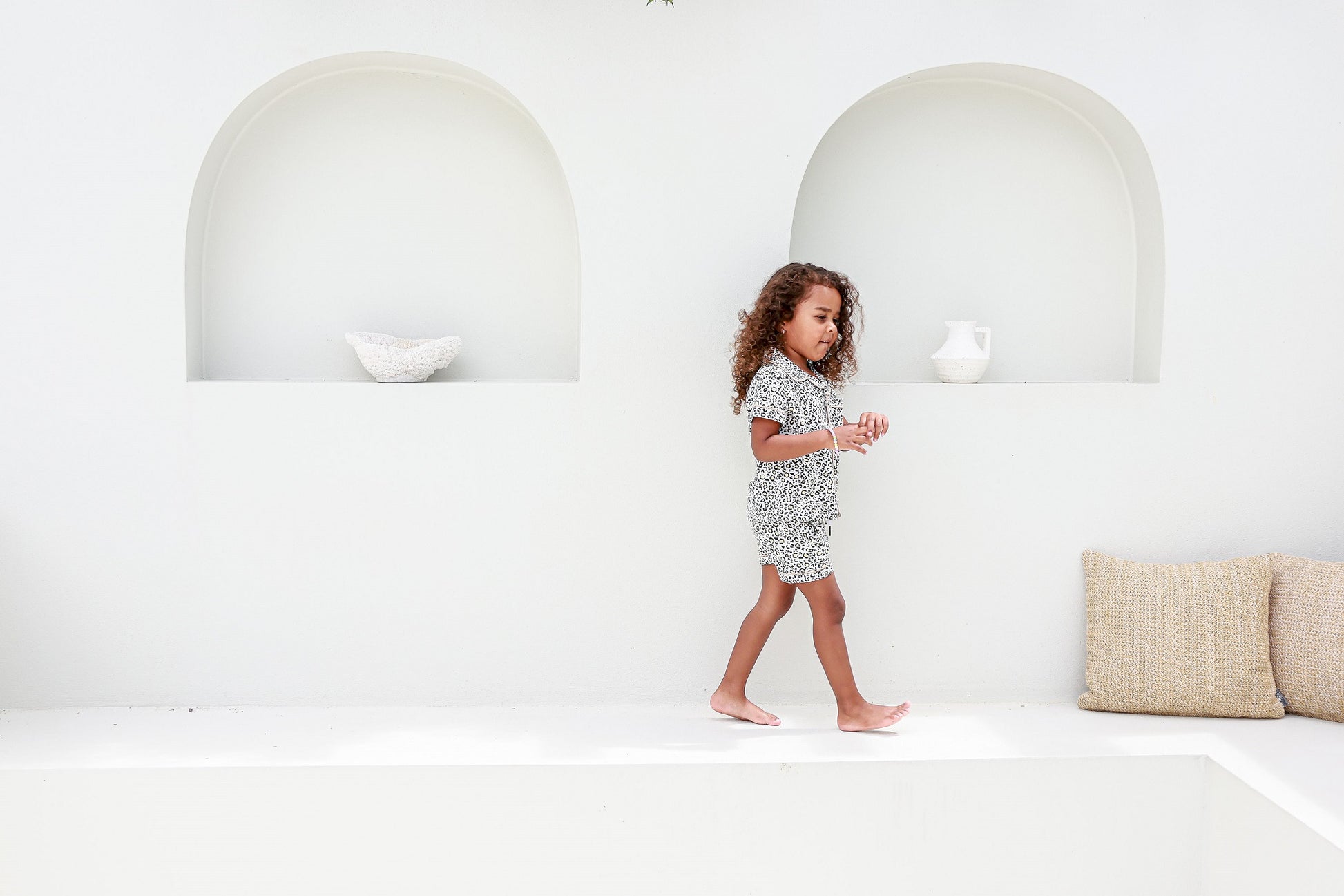 Girl walking past a white arched wall, wearing piped leopard print pajamas, combining style and comfort.