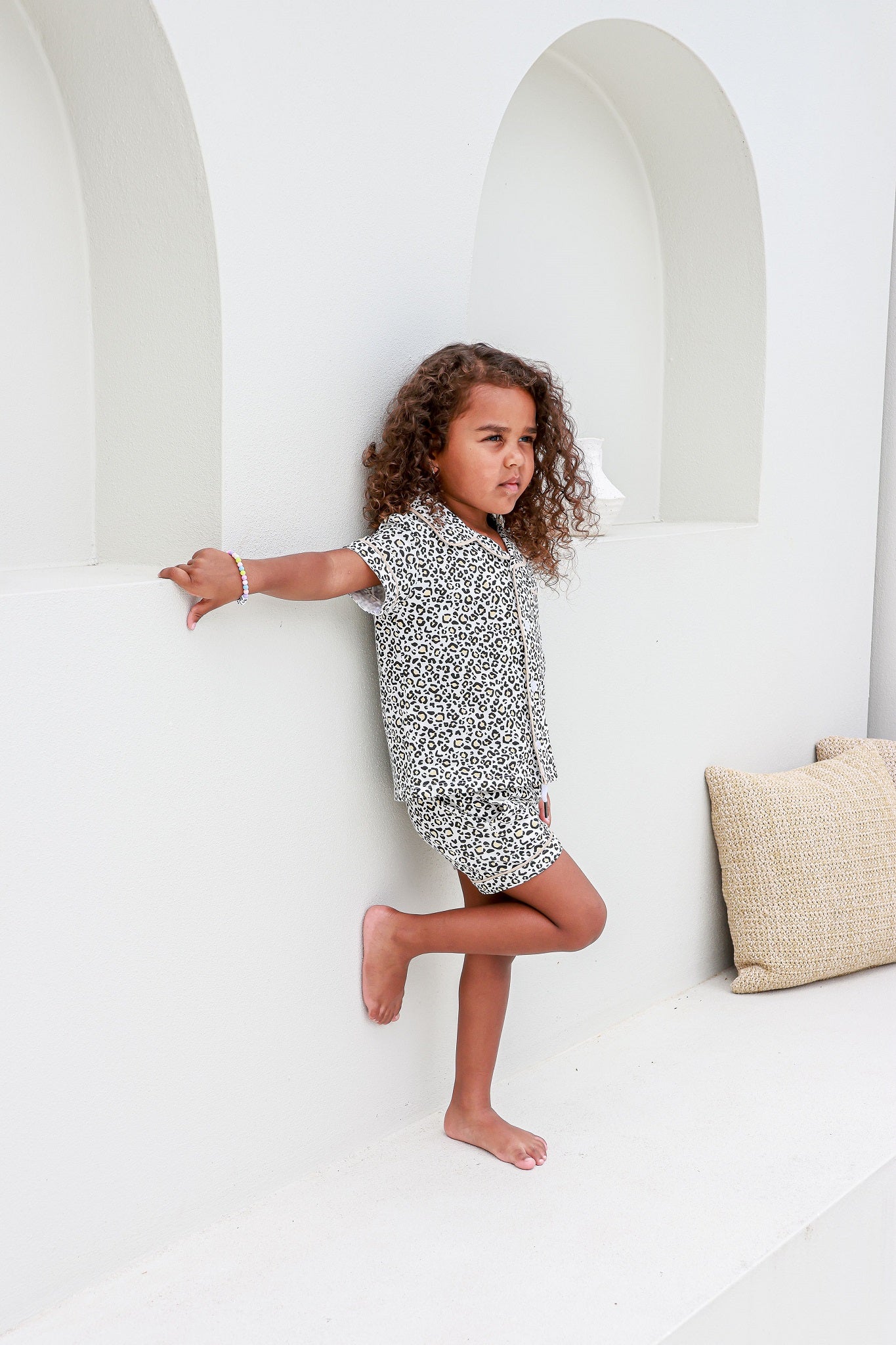 Toddler girl leaning on white arched wall wearing leopard print piped pyjama sets pj's pajamas