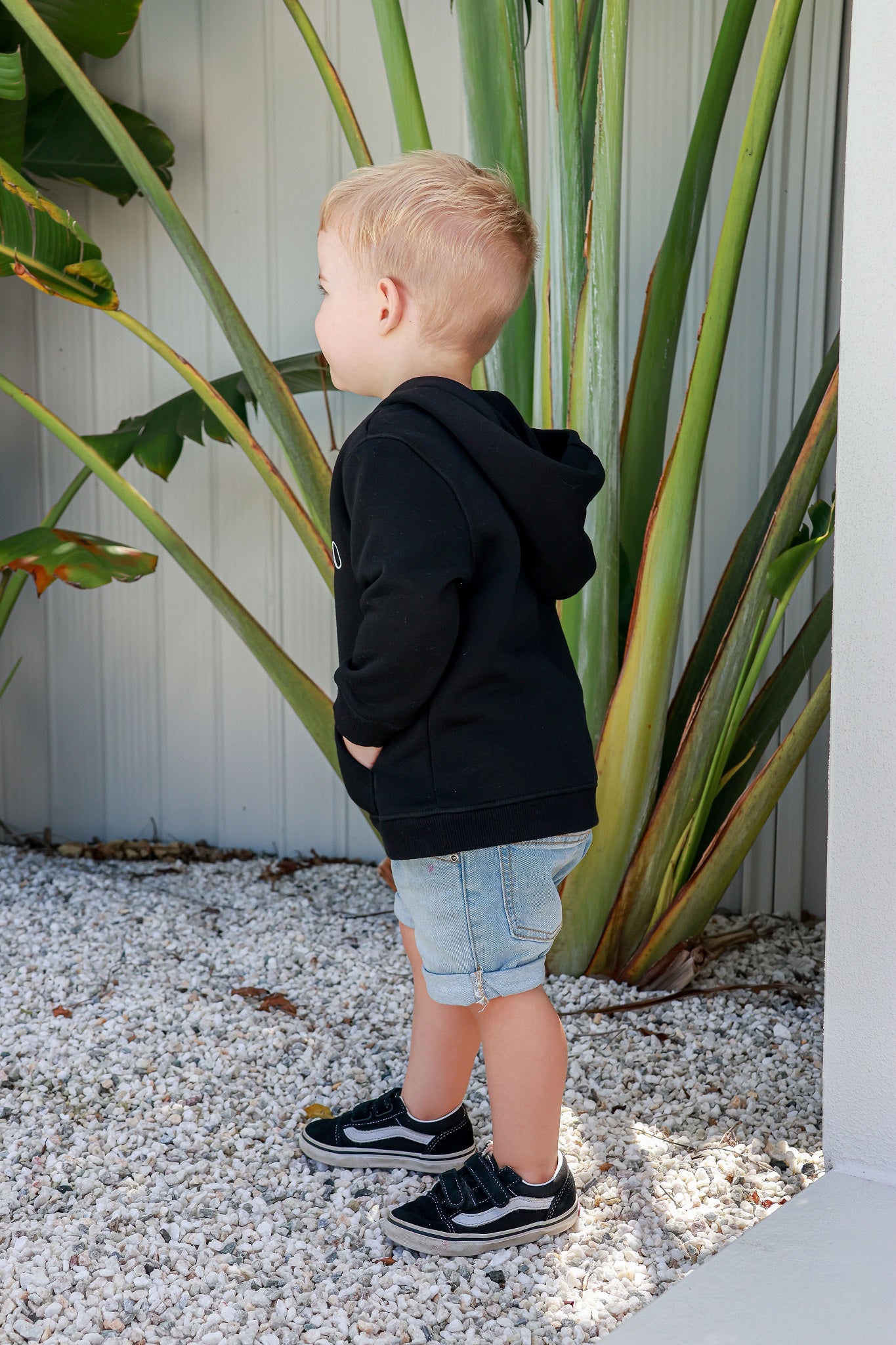 Toddler boy standing outside and smiling wearing black logo jumper 