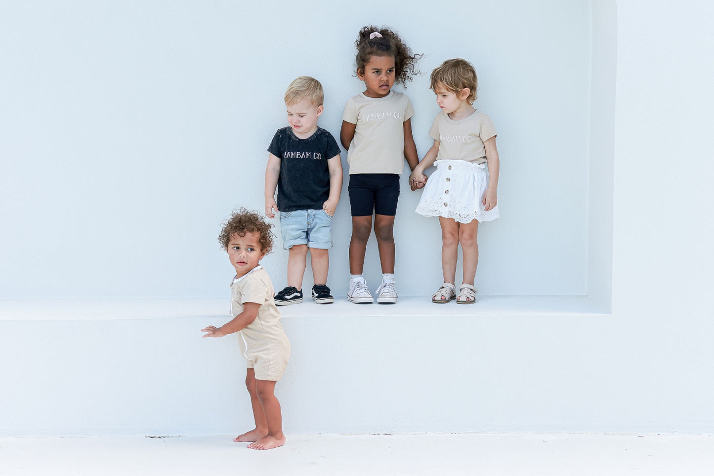 Kids all wearing matching logo appeal standing against white backdrop on a step