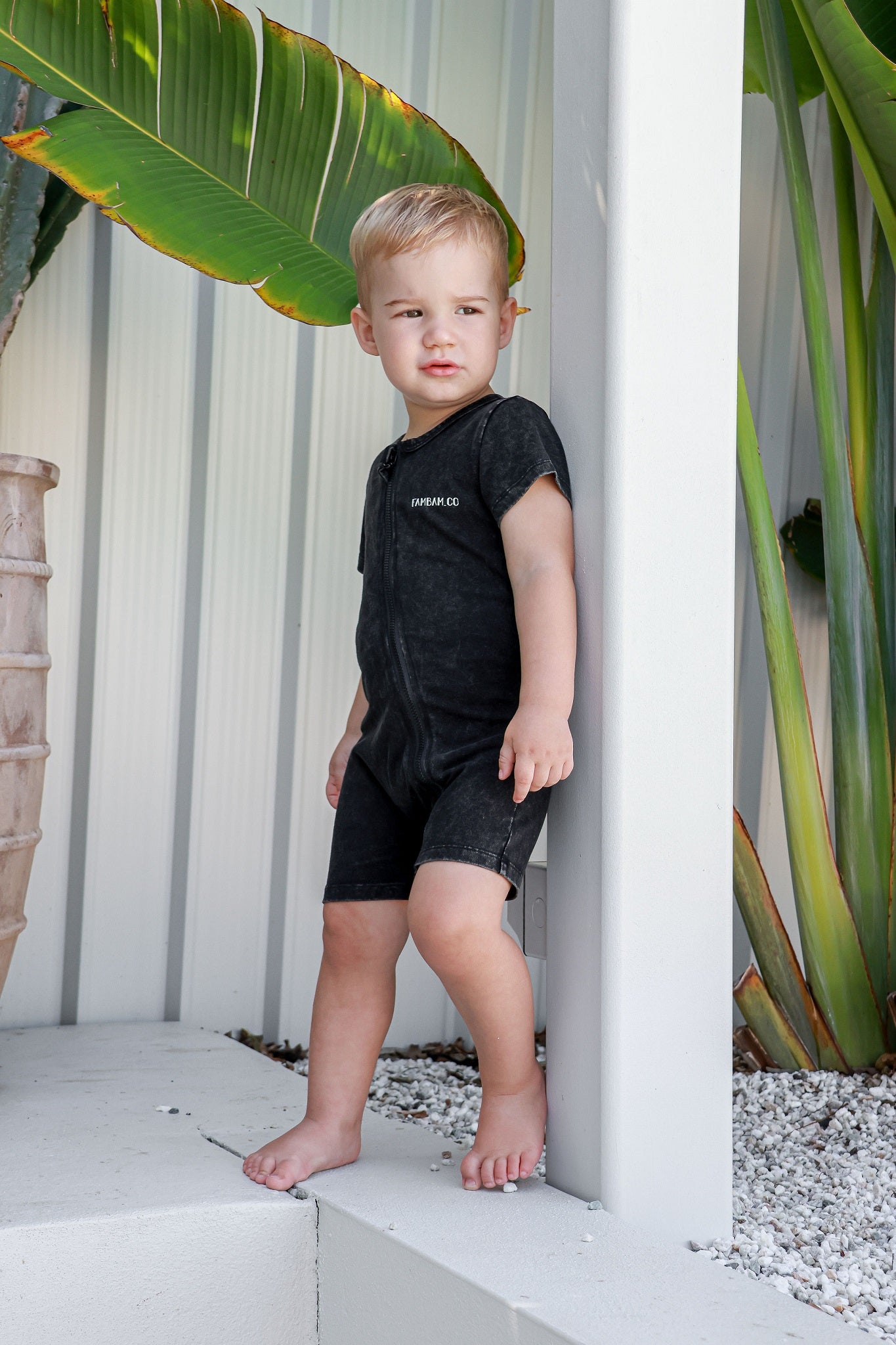 Boy toddler in logo acid wash romper leaning on post