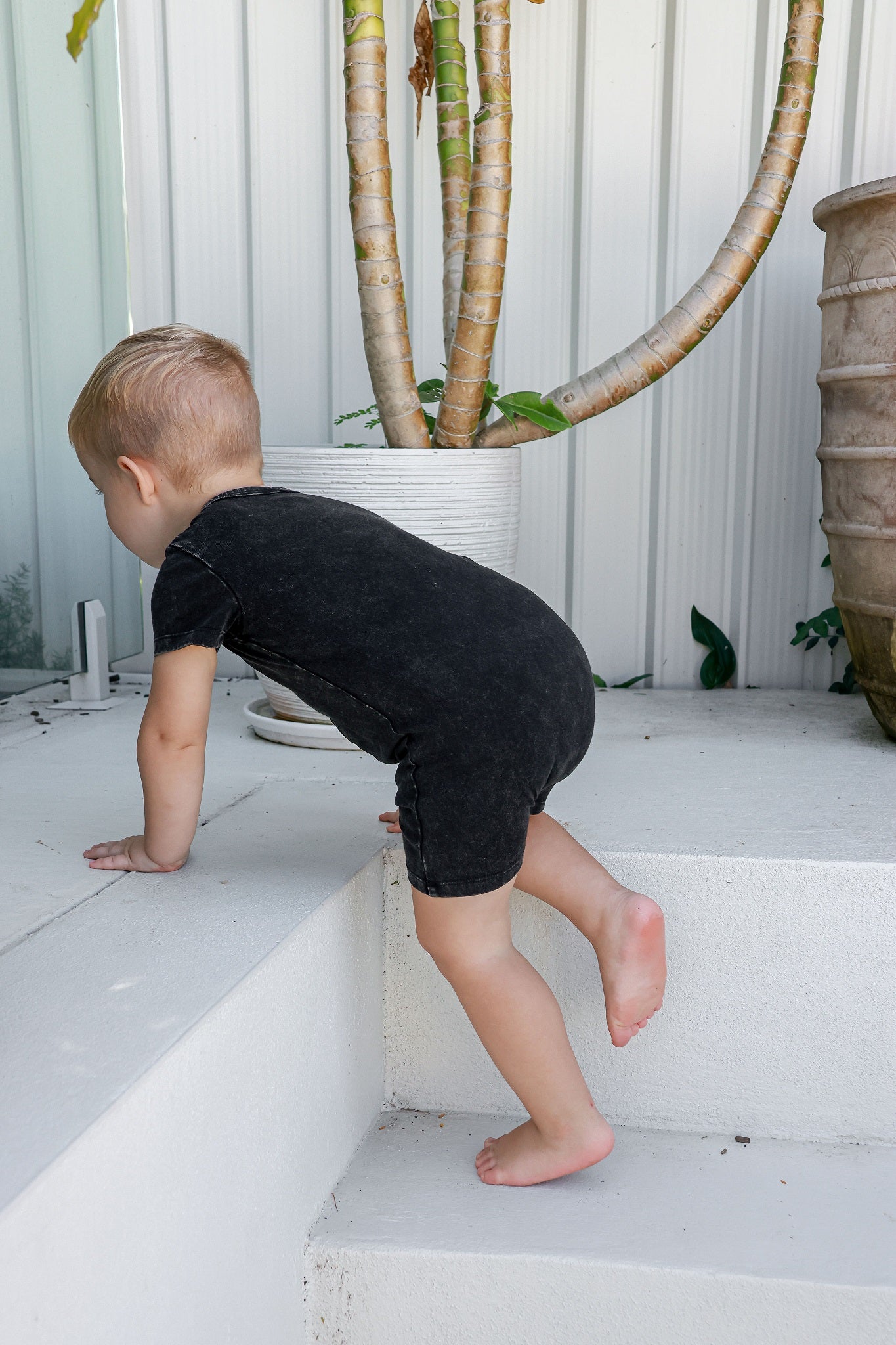 Boy toddler in logo acid wash romper climbing up steps